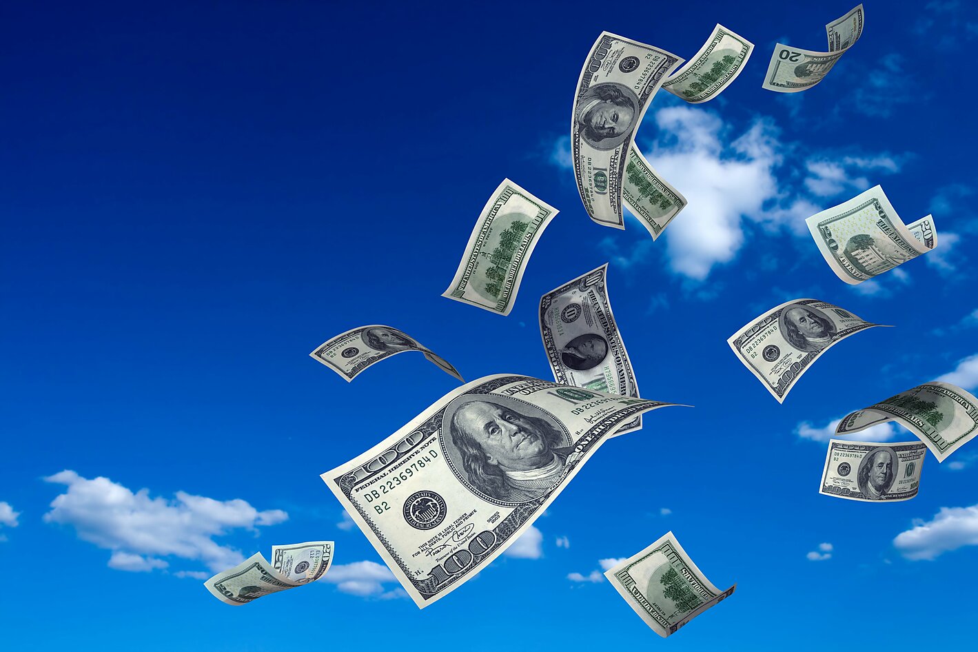 Hundred dollar bills flying in the wind against a blue sky