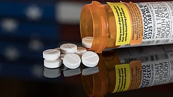 A bottle of prescription oxycodone, open on a table with an American flag in the background